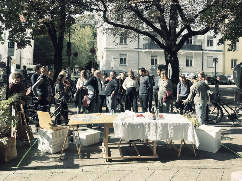 Ein Gruppe Menschen steht vor einem Esstisch, der auf der Straße aufgebaut ist.