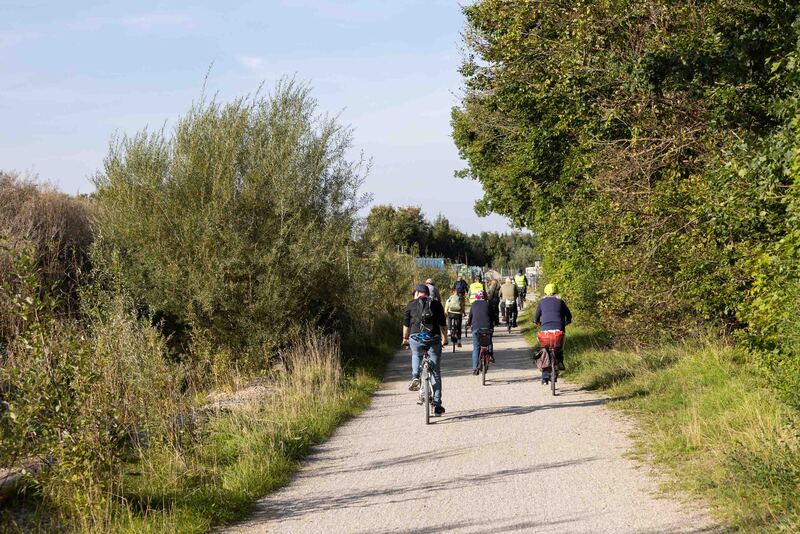 Eine Gruppe Radfahrer*innen fährt auf einem Schotterweg durch die Parkmeile Trudering-Neuperlach.